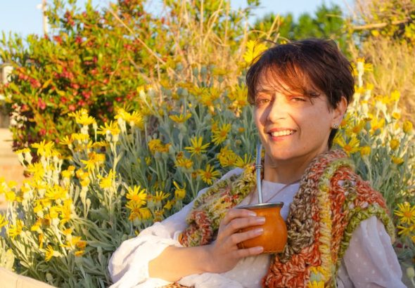 A woman smiles while drinking traditional mate among yellow flowers in Montevideo.